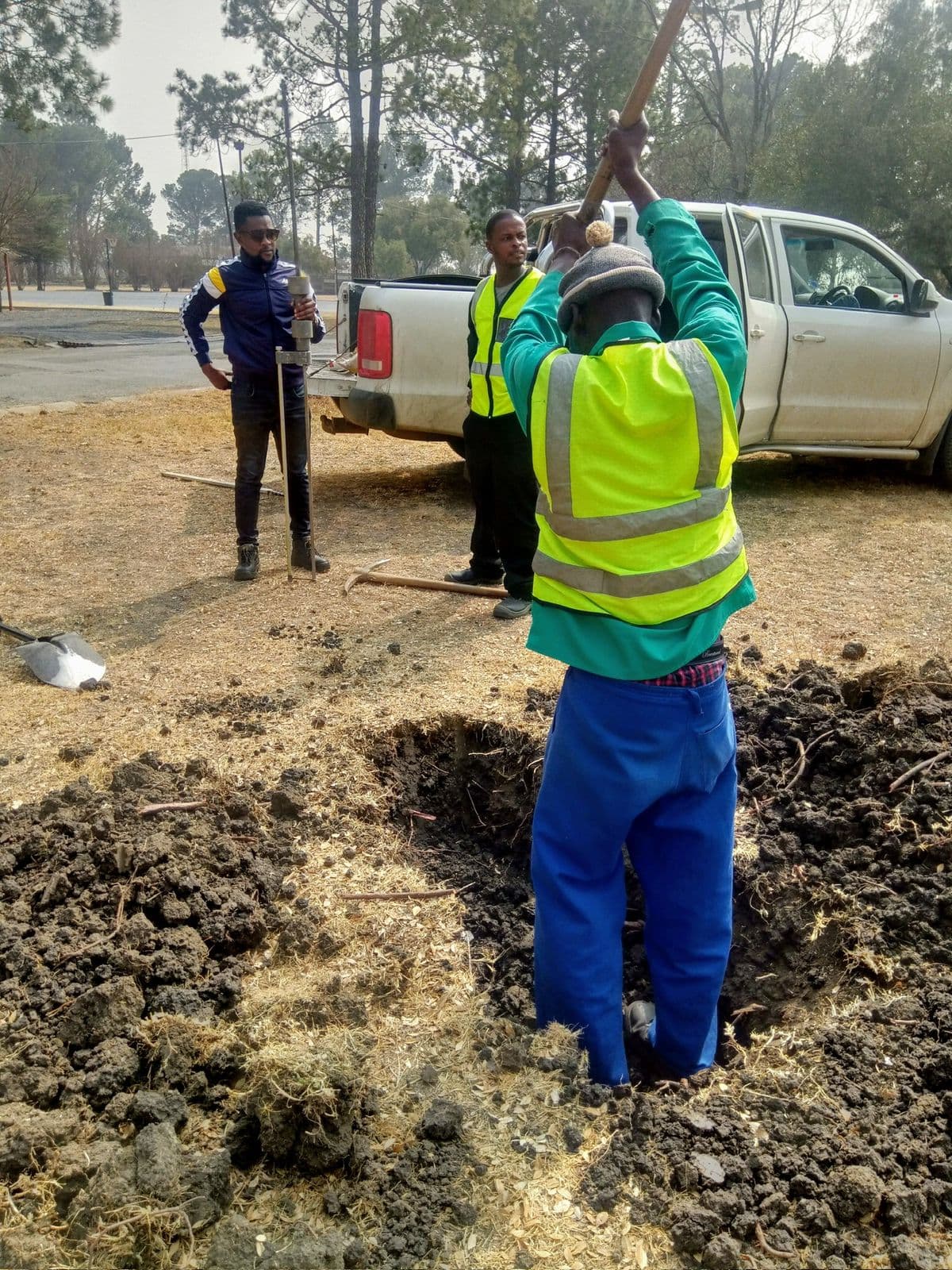 Mbozisi team breaking ground and measuring soil conditions beside a pickup truck.