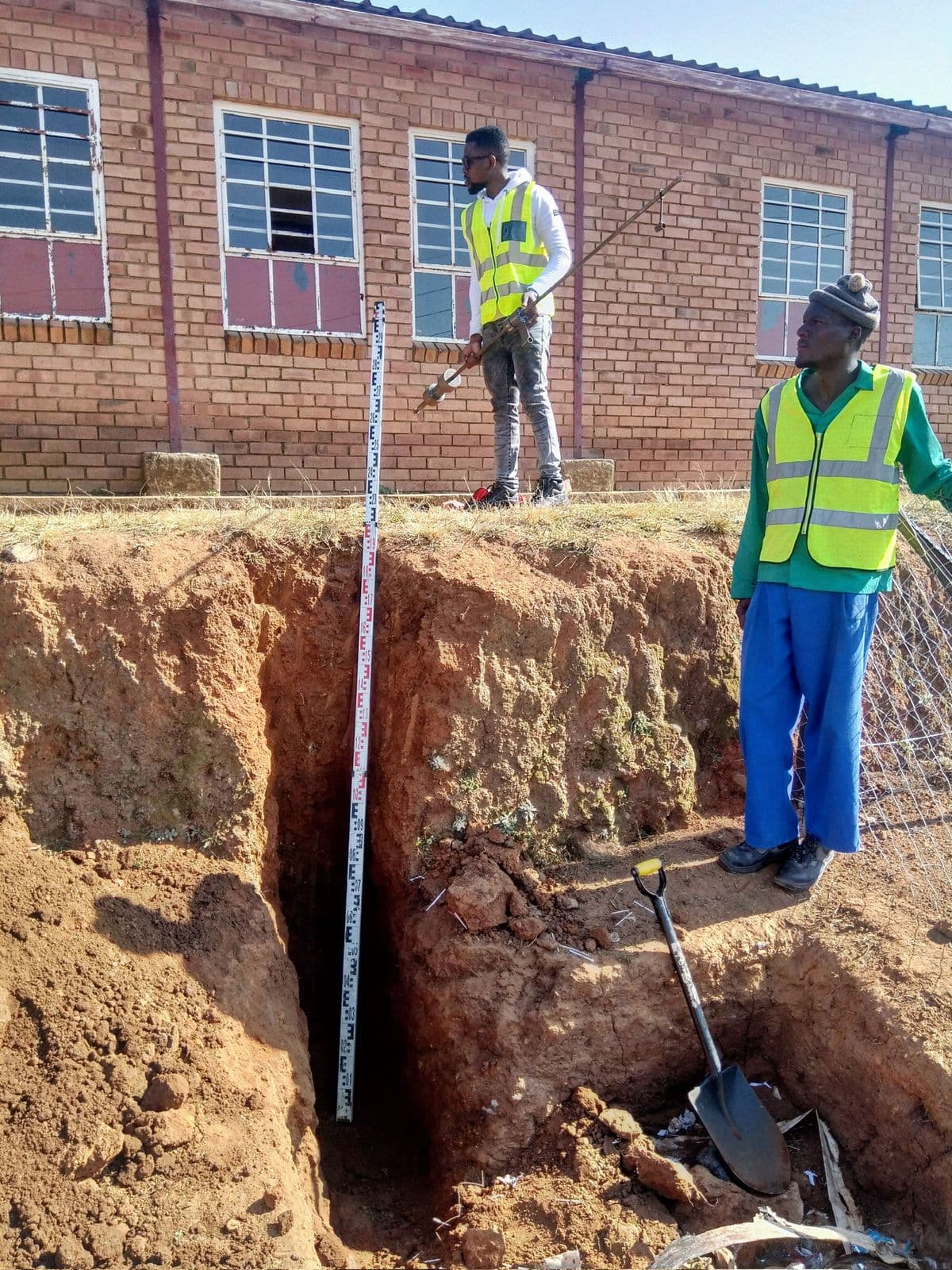 Survey crew checking ground levels and depth beside a trench on site.