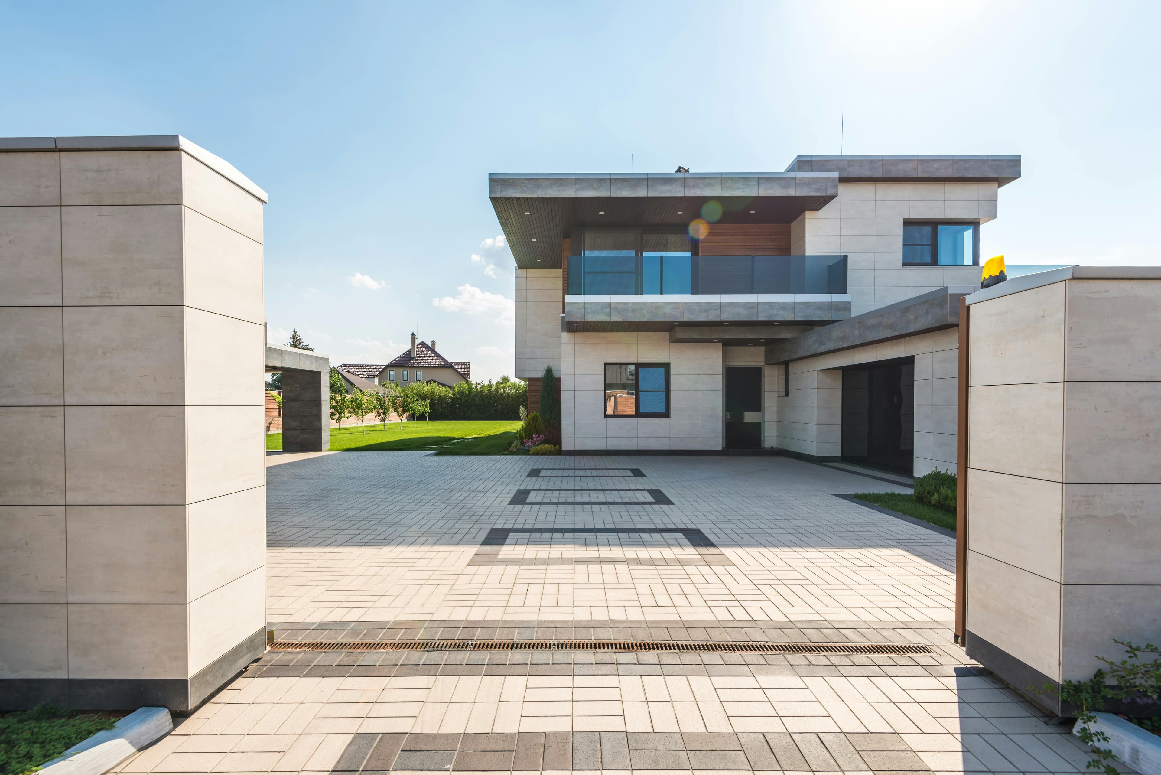 Modern two-story residential house with a paved driveway, clean lines, and large windows.